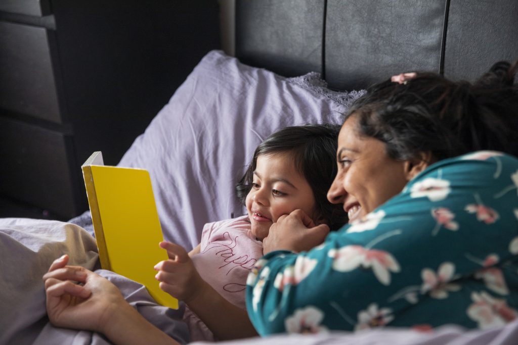 Mother and young daughter reading a book together in bed as part of a calm bedtime routine