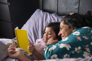 Mother and young daughter reading a book together in bed as part of a calm bedtime routine
